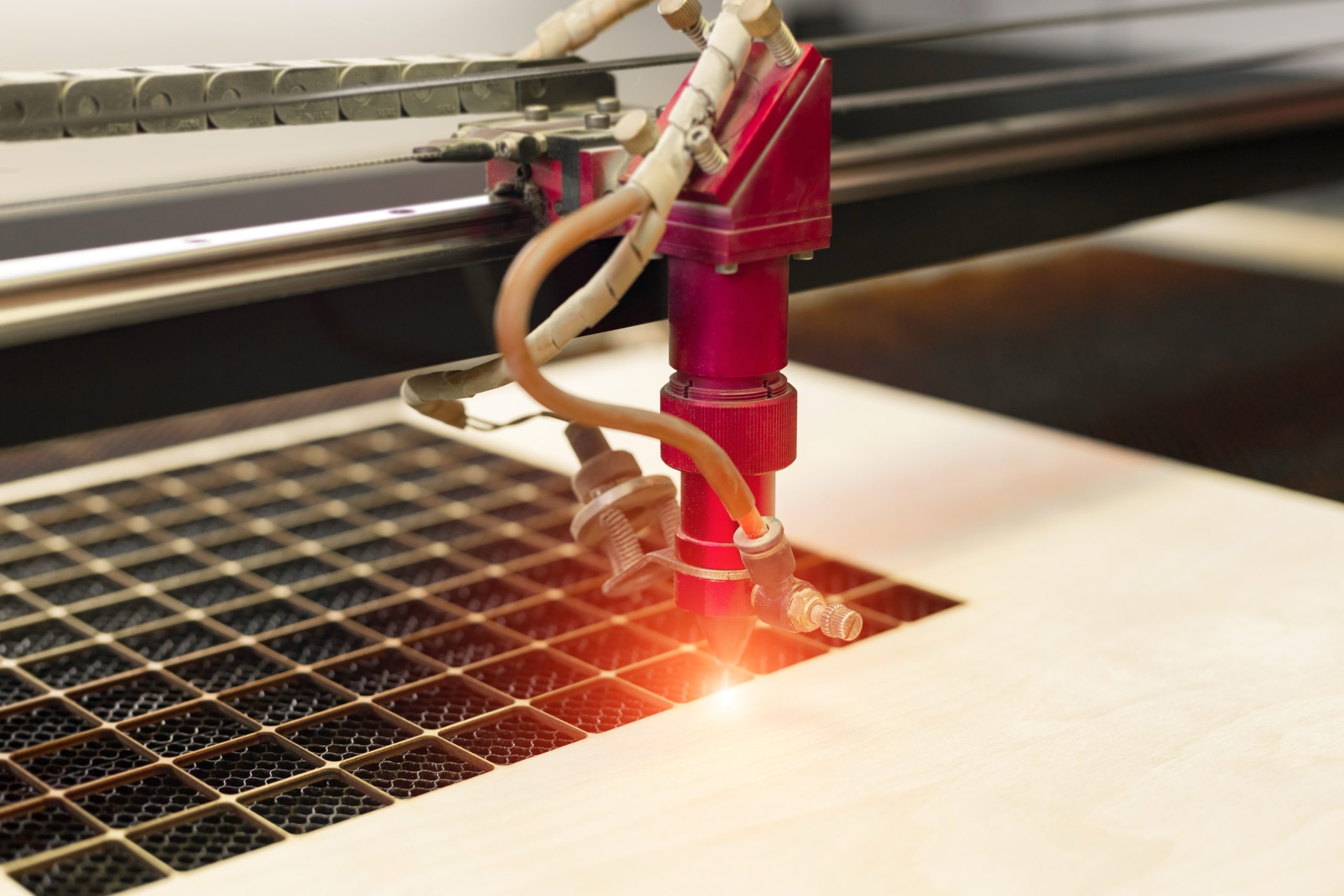 CO2 laser cutting machine is precisely cutting a piece of light brown wood.
