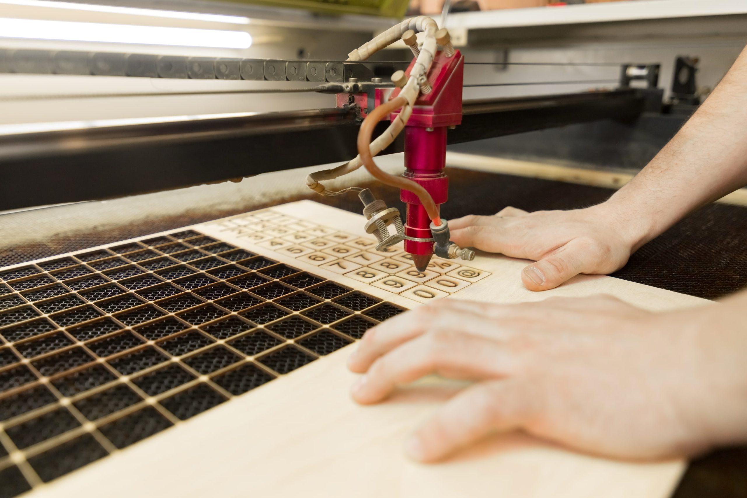 A worker uses a laser cutting machine to engrave letters on a sheet of wood.
